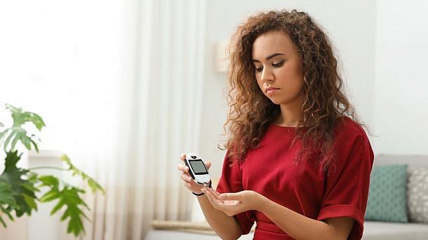 Young African-American woman using digital glucometer at home. Diabetes control
